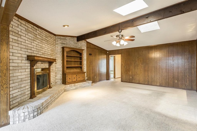 unfurnished living room featuring built in features, carpet, vaulted ceiling with skylight, wood walls, and a brick fireplace