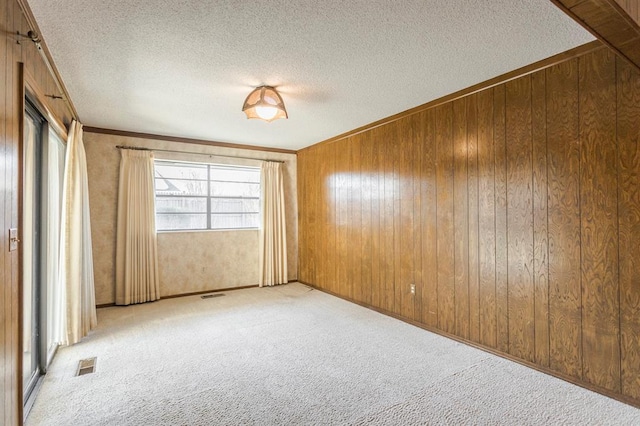 carpeted empty room with wooden walls, ornamental molding, visible vents, and a textured ceiling