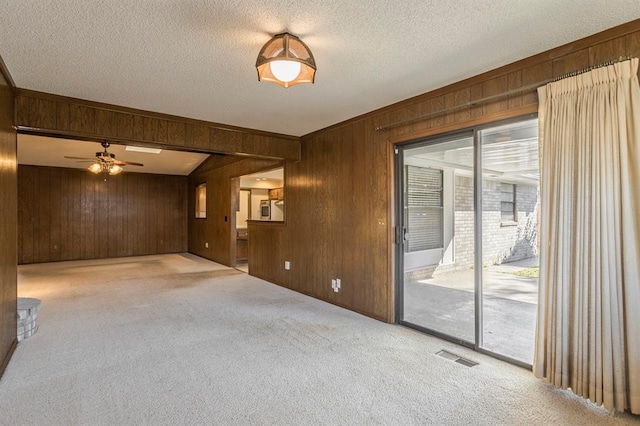 spare room featuring carpet flooring, visible vents, wood walls, and a textured ceiling