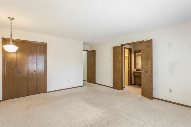 unfurnished bedroom featuring ensuite bath, light colored carpet, baseboards, and a textured ceiling