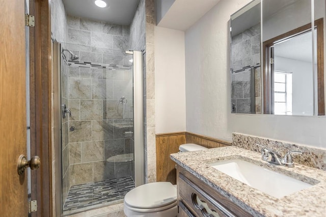 bathroom featuring wooden walls, a shower stall, toilet, wainscoting, and vanity