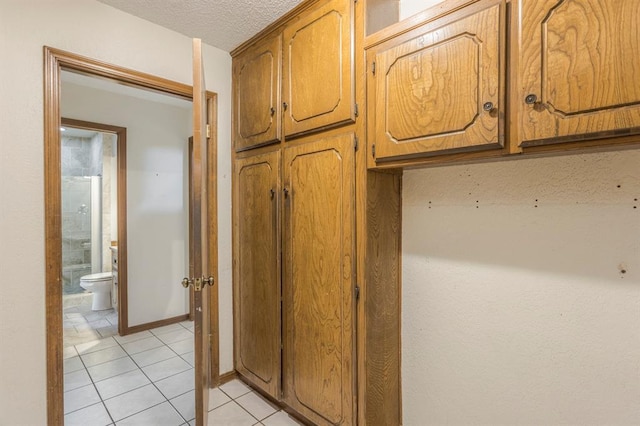 kitchen featuring light tile patterned flooring, brown cabinetry, baseboards, and a textured ceiling