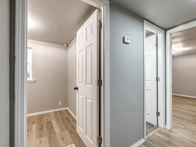 corridor featuring light wood finished floors and baseboards