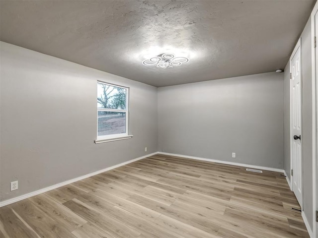 spare room featuring light wood-style flooring, a textured ceiling, and baseboards