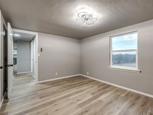 spare room with baseboards, light wood finished floors, and a textured ceiling