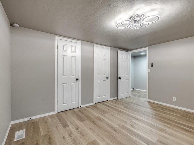 interior space featuring visible vents, baseboards, light wood finished floors, and a textured ceiling