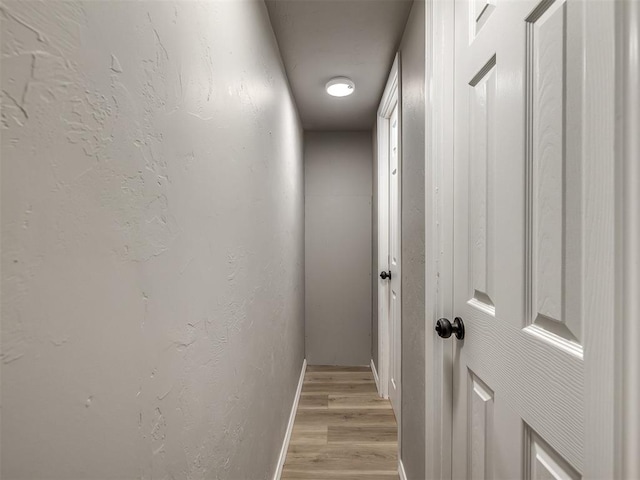 hall featuring light wood finished floors, baseboards, and a textured wall