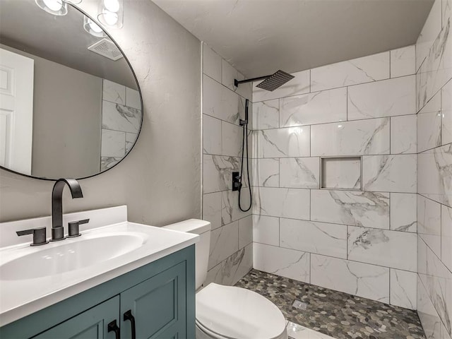 bathroom featuring vanity, toilet, visible vents, and tiled shower