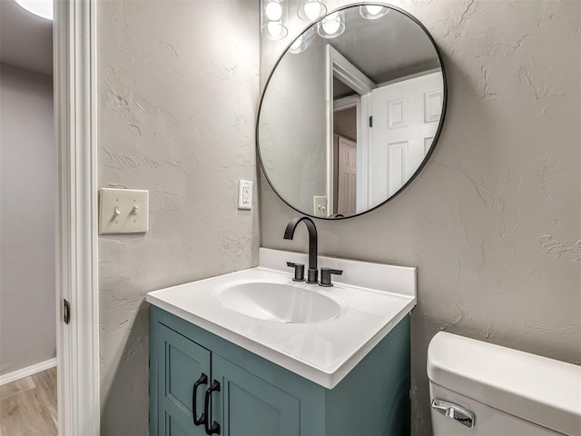 bathroom featuring wood finished floors, toilet, vanity, and a textured wall