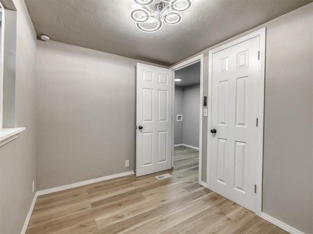 interior space with a textured ceiling, visible vents, light wood-type flooring, and baseboards