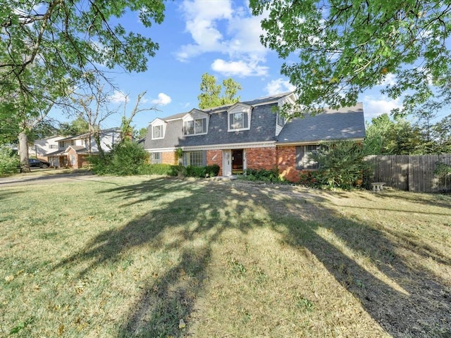 dutch colonial featuring brick siding, a shingled roof, a front yard, and fence