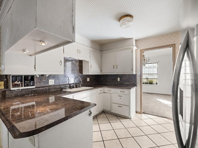 kitchen with a peninsula, freestanding refrigerator, a sink, light carpet, and white cabinetry