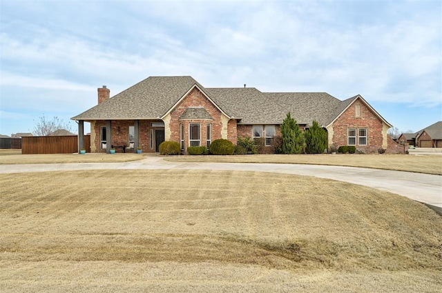 view of front of home with brick siding, curved driveway, a shingled roof, fence, and a chimney