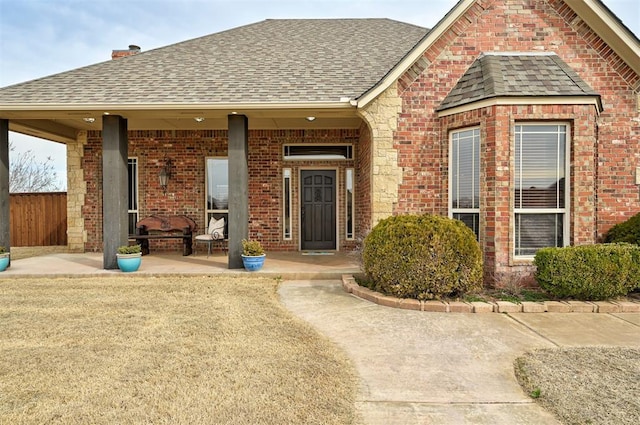 view of front of house featuring covered porch, brick siding, and roof with shingles