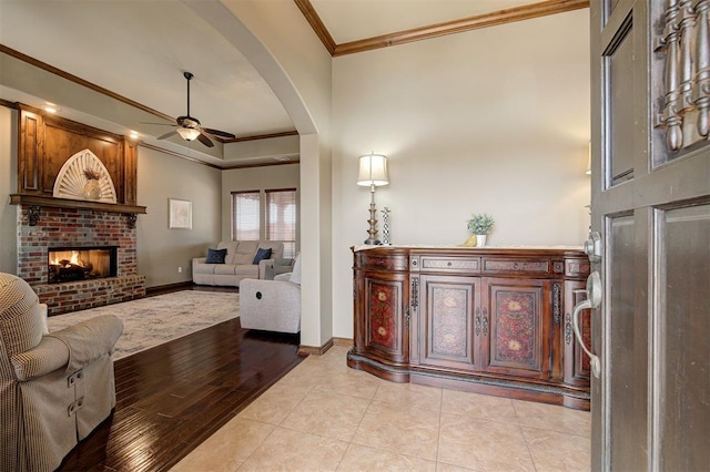 living area featuring ornamental molding, a ceiling fan, arched walkways, a fireplace, and baseboards