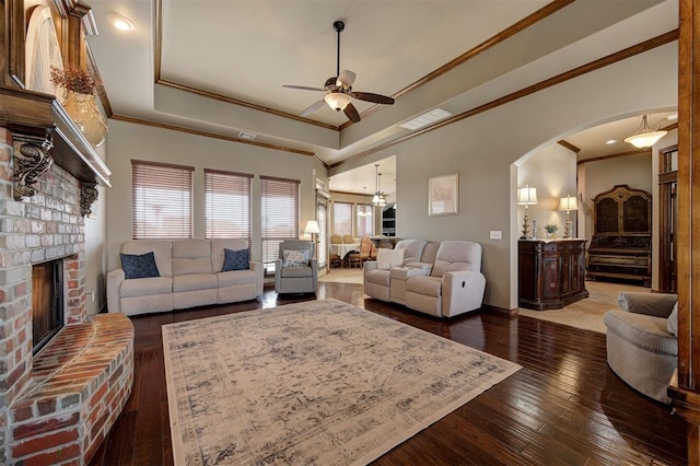 living room with ceiling fan, a tray ceiling, a fireplace, hardwood / wood-style flooring, and arched walkways