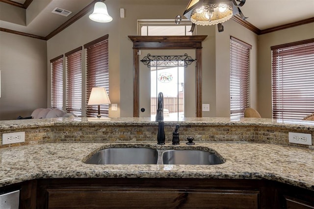 kitchen with crown molding, light stone counters, visible vents, and a sink