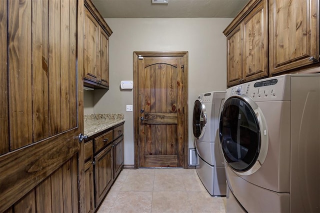 clothes washing area featuring separate washer and dryer, light tile patterned floors, and cabinet space