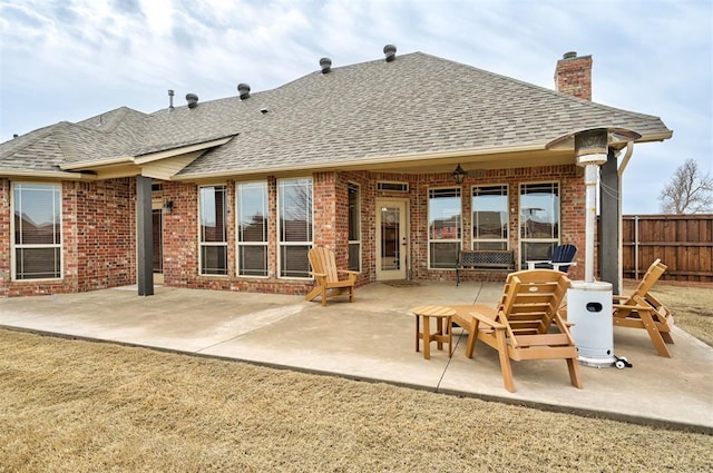 rear view of property featuring fence, a patio area, brick siding, and roof with shingles