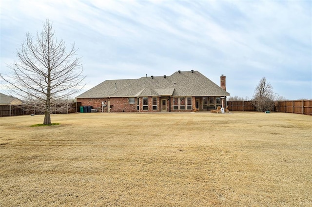 rear view of house with brick siding, a lawn, a chimney, and fence