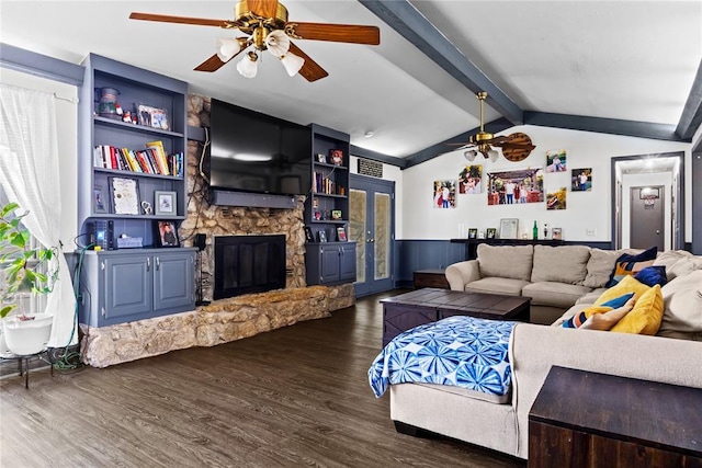 living room with dark wood finished floors, a stone fireplace, wainscoting, ceiling fan, and vaulted ceiling with beams