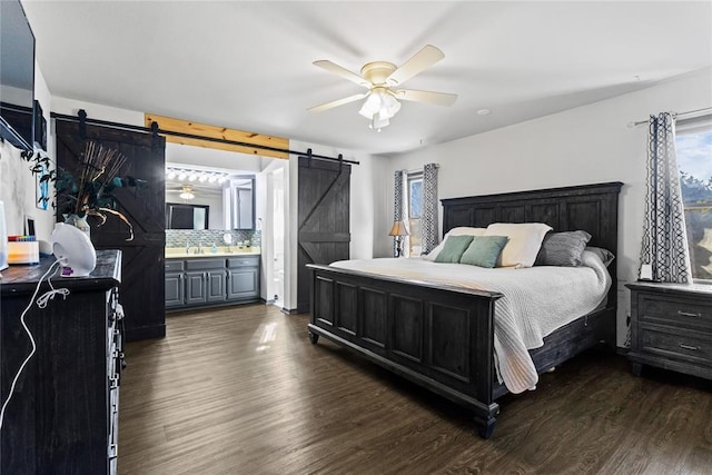 bedroom with a barn door, a ceiling fan, dark wood-type flooring, and a sink