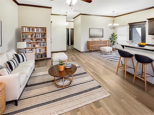 living room with visible vents, ceiling fan with notable chandelier, ornamental molding, and light wood finished floors