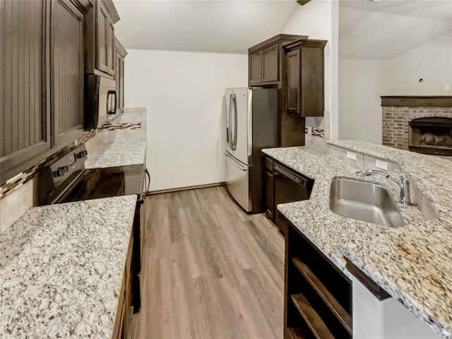 kitchen with light stone counters, a sink, dark brown cabinets, stainless steel refrigerator with ice dispenser, and light wood-type flooring