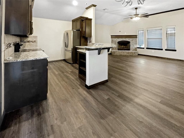 kitchen with a breakfast bar area, dark wood finished floors, freestanding refrigerator, vaulted ceiling, and open floor plan