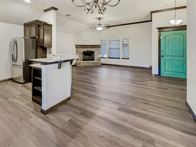 kitchen with a brick fireplace, pendant lighting, lofted ceiling, freestanding refrigerator, and wood finished floors