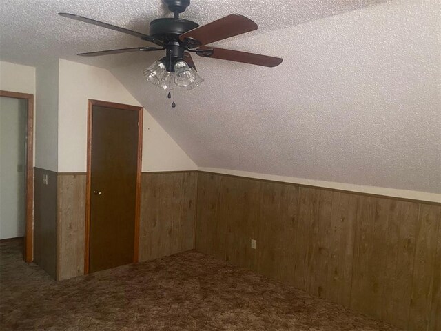 additional living space featuring wooden walls, carpet, a wainscoted wall, lofted ceiling, and a textured ceiling