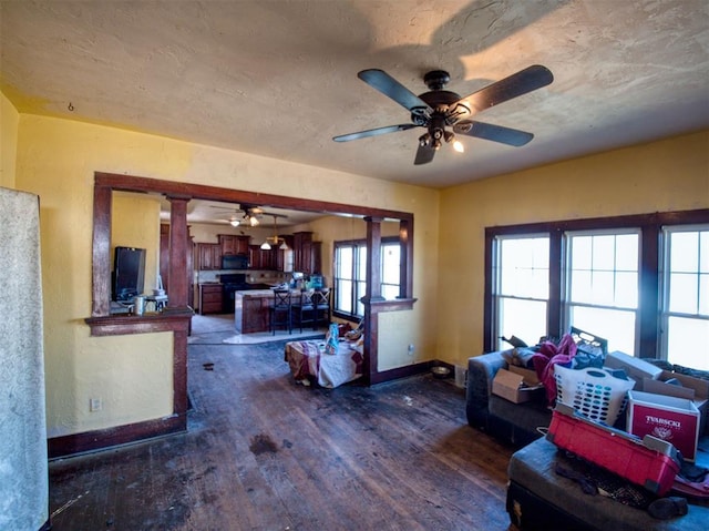 living room with a ceiling fan, a textured ceiling, decorative columns, baseboards, and dark wood-style flooring