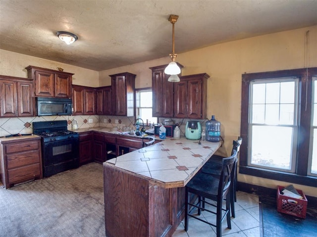 kitchen with a peninsula, a sink, decorative backsplash, black appliances, and a kitchen bar