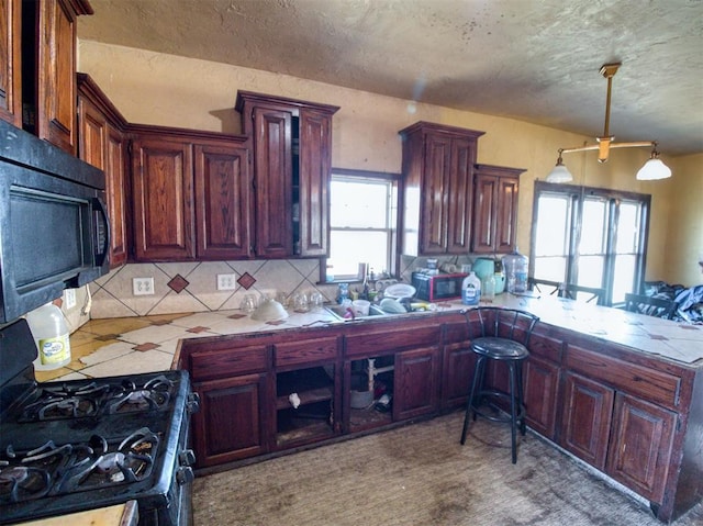 kitchen with backsplash, light countertops, a peninsula, black appliances, and a sink