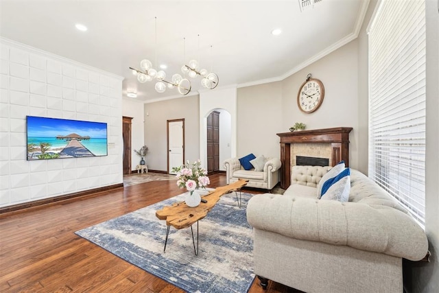 living room featuring wood finished floors, arched walkways, an inviting chandelier, a fireplace, and crown molding