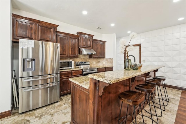 kitchen with light stone counters, visible vents, stainless steel appliances, under cabinet range hood, and backsplash