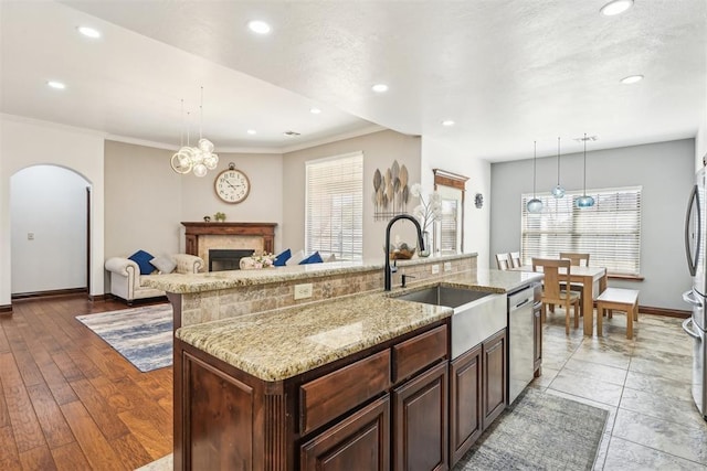 kitchen with an island with sink, a sink, light stone counters, arched walkways, and appliances with stainless steel finishes