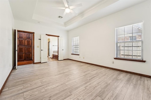 unfurnished bedroom featuring visible vents, ensuite bathroom, a tray ceiling, light wood finished floors, and baseboards