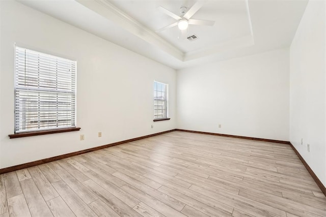 spare room with a ceiling fan, visible vents, baseboards, light wood-style flooring, and a raised ceiling