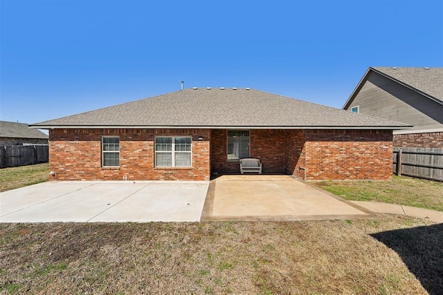 rear view of property with a fenced backyard, a shingled roof, a lawn, a patio area, and brick siding