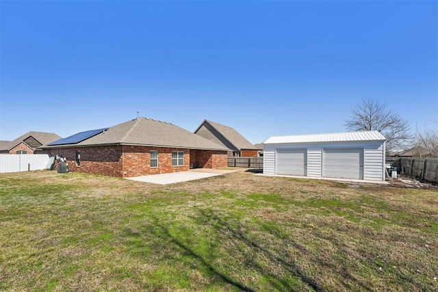 back of property featuring a detached garage, a yard, an outdoor structure, a fenced backyard, and a patio