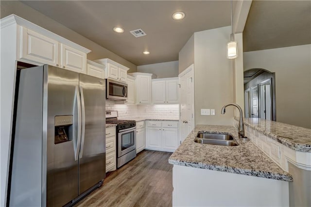 kitchen featuring a sink, wood finished floors, white cabinetry, appliances with stainless steel finishes, and a peninsula