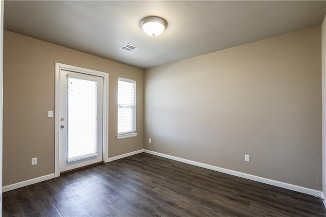 spare room featuring visible vents, baseboards, and dark wood finished floors