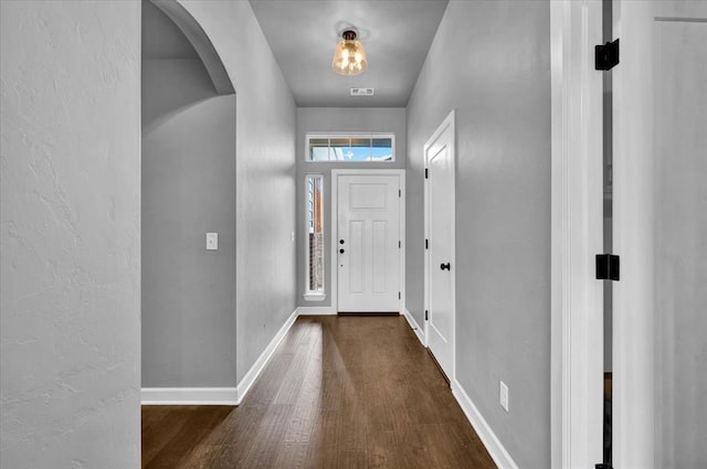 doorway to outside featuring arched walkways, visible vents, baseboards, and wood finished floors