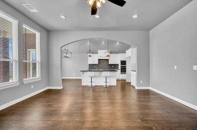 unfurnished living room with visible vents, baseboards, dark wood finished floors, arched walkways, and a ceiling fan