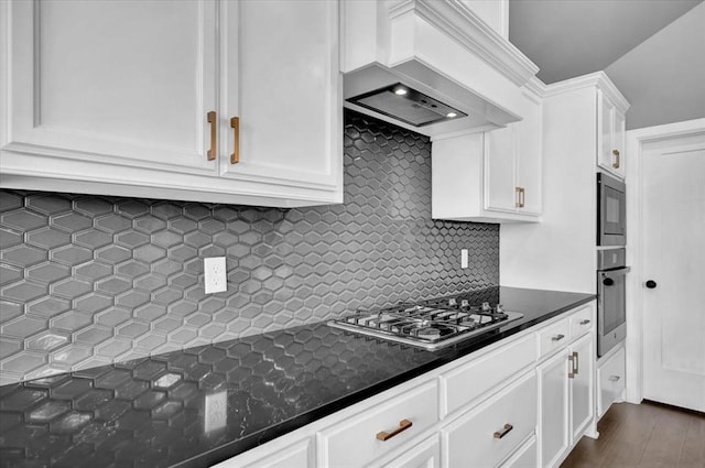 kitchen featuring dark stone countertops, backsplash, appliances with stainless steel finishes, white cabinets, and custom exhaust hood