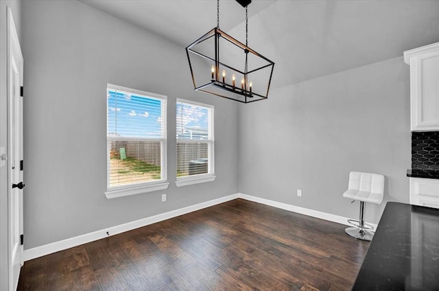 unfurnished dining area featuring dark wood-style floors, baseboards, lofted ceiling, and an inviting chandelier