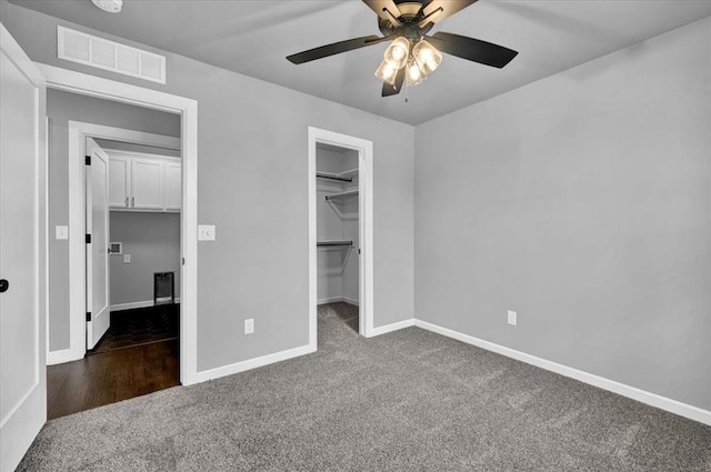 unfurnished bedroom featuring a spacious closet, visible vents, baseboards, carpet, and a ceiling fan