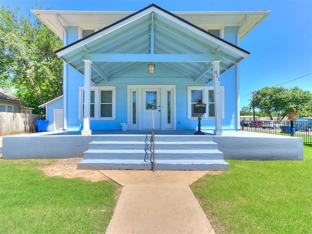 view of front of home with covered porch, a front lawn, and fence