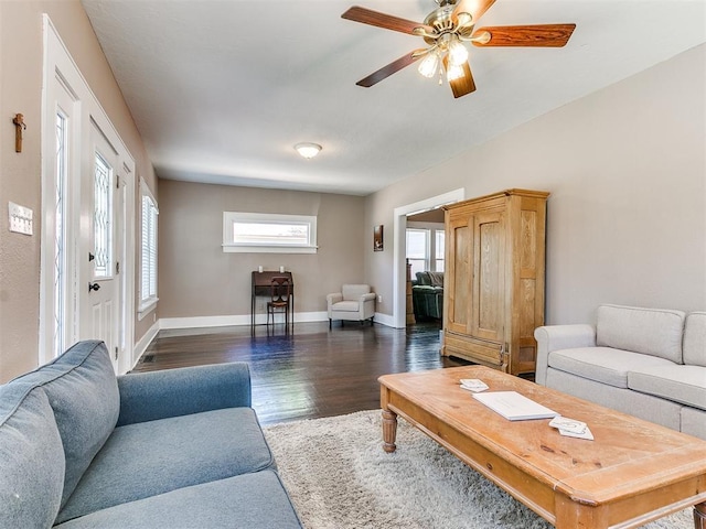 living area featuring baseboards, dark wood-type flooring, and a ceiling fan